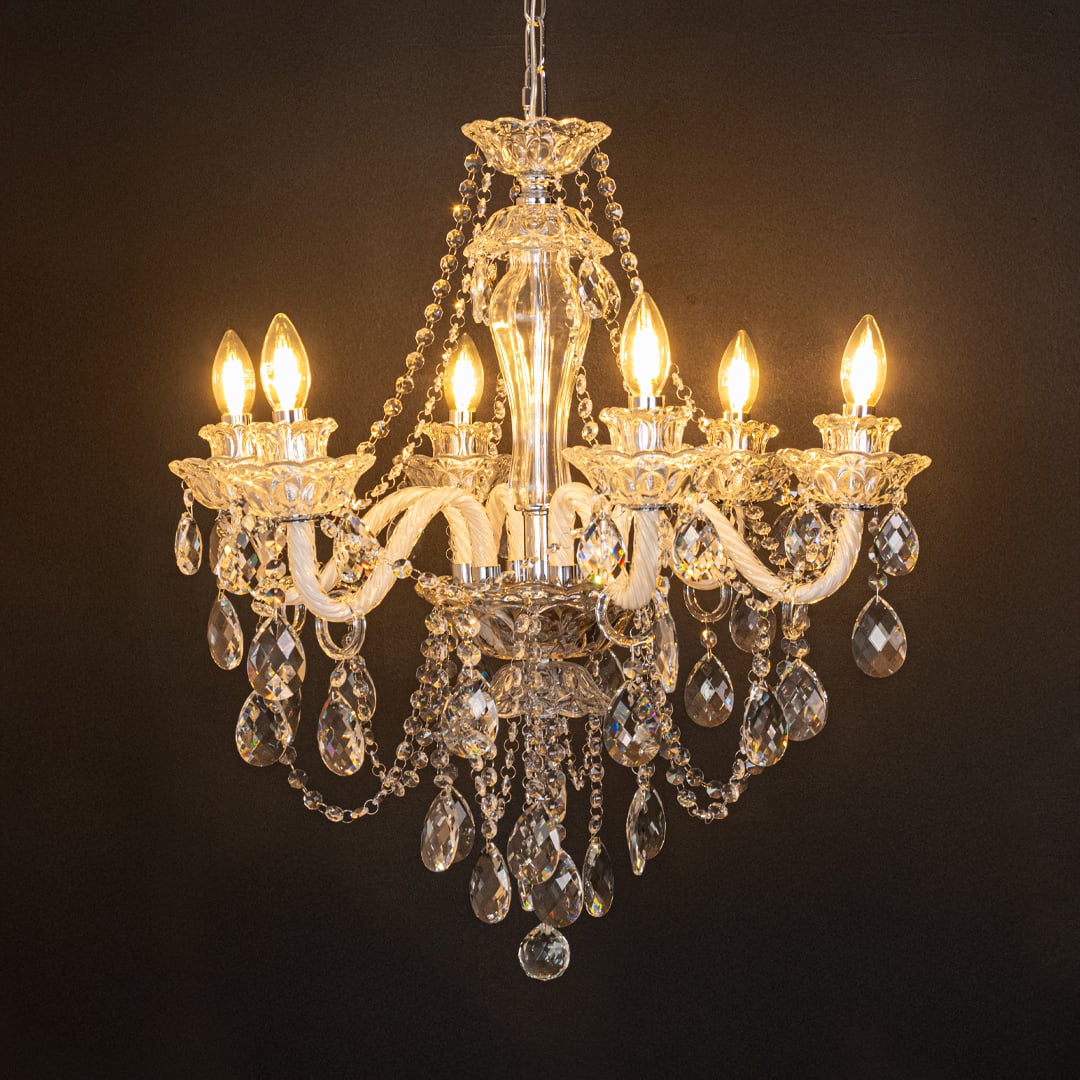 Clear crystal chandelier glowing warmly on black background creating a dramatic luxury ceiling feature.