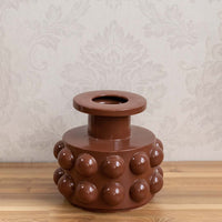 Brown ceramic decorative vase with bubble detailing styled on a wooden table for warm modern home decor displays.