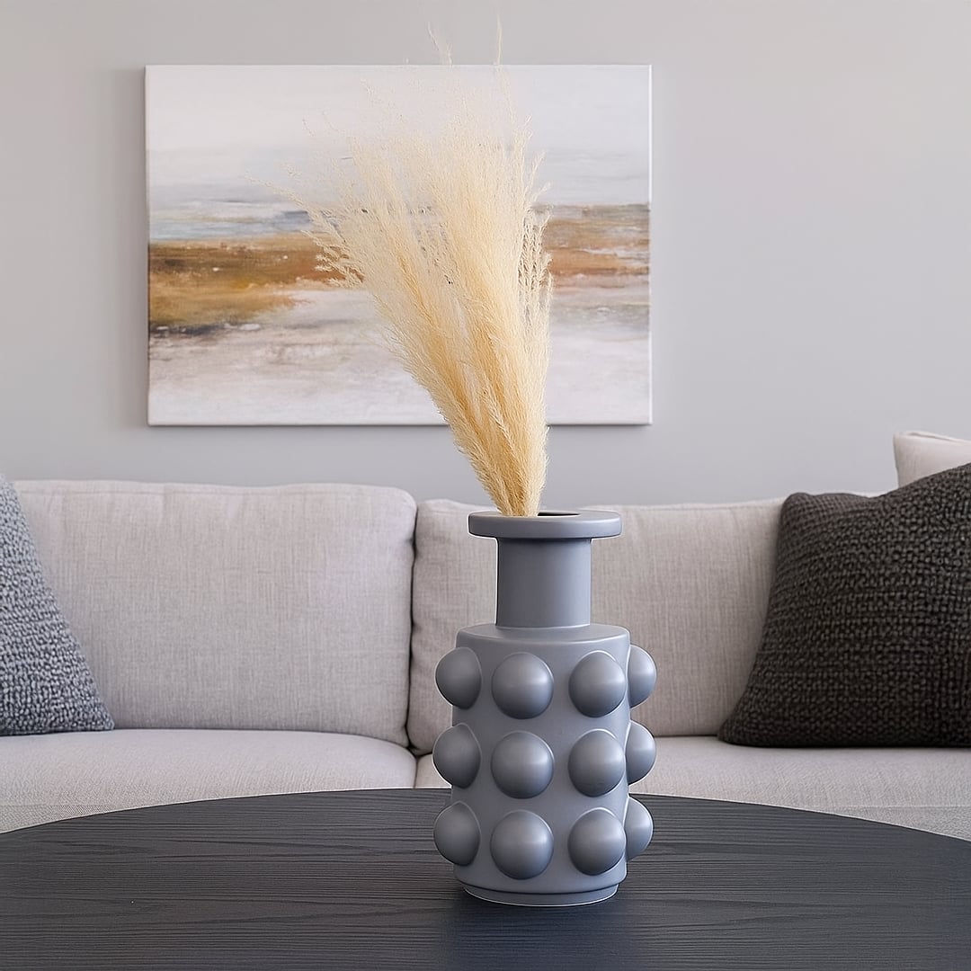 A modern grey sculptural vase with bold raised sphere detailing styled in a soft setting offering a clean minimal decorative look for interiors.