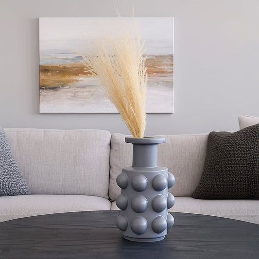 A modern grey sculptural vase with bold raised sphere detailing styled in a soft setting offering a clean minimal decorative look for interiors.