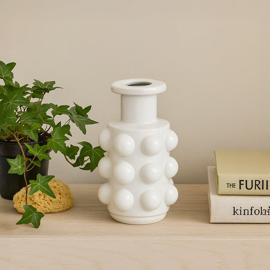 White bubble ceramic vase styled on a wooden shelf beside green ivy and stacked books for a modern home decor look.