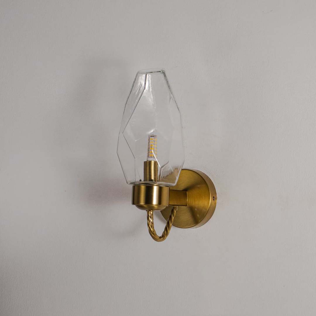 Wall sconce with geometric clear glass shade and gold finish base perfect for modern bedroom living room and hallway interiors.