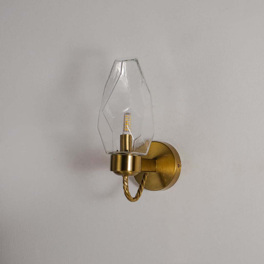 Wall sconce with geometric clear glass shade and gold finish base perfect for modern bedroom living room and hallway interiors.