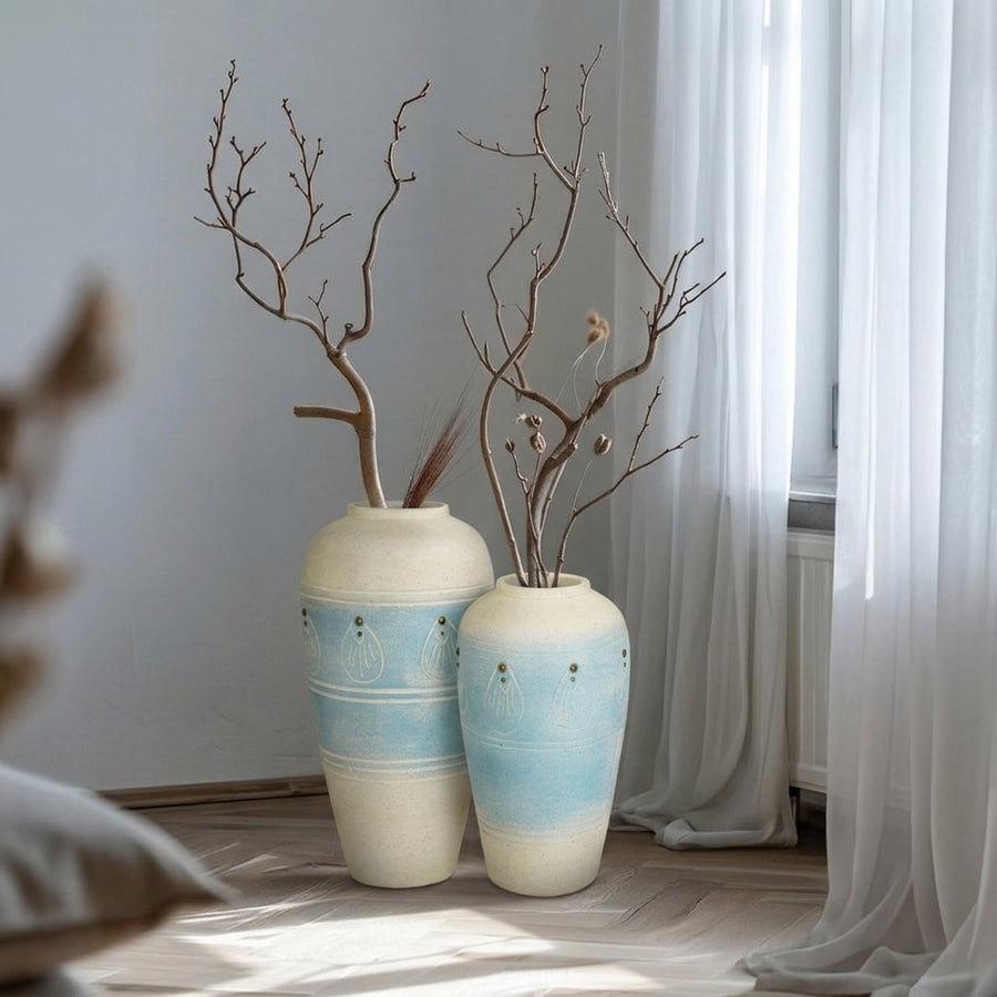 Beige and blue ceramic floor vases with branches placed near curtain for modern home decor styling.