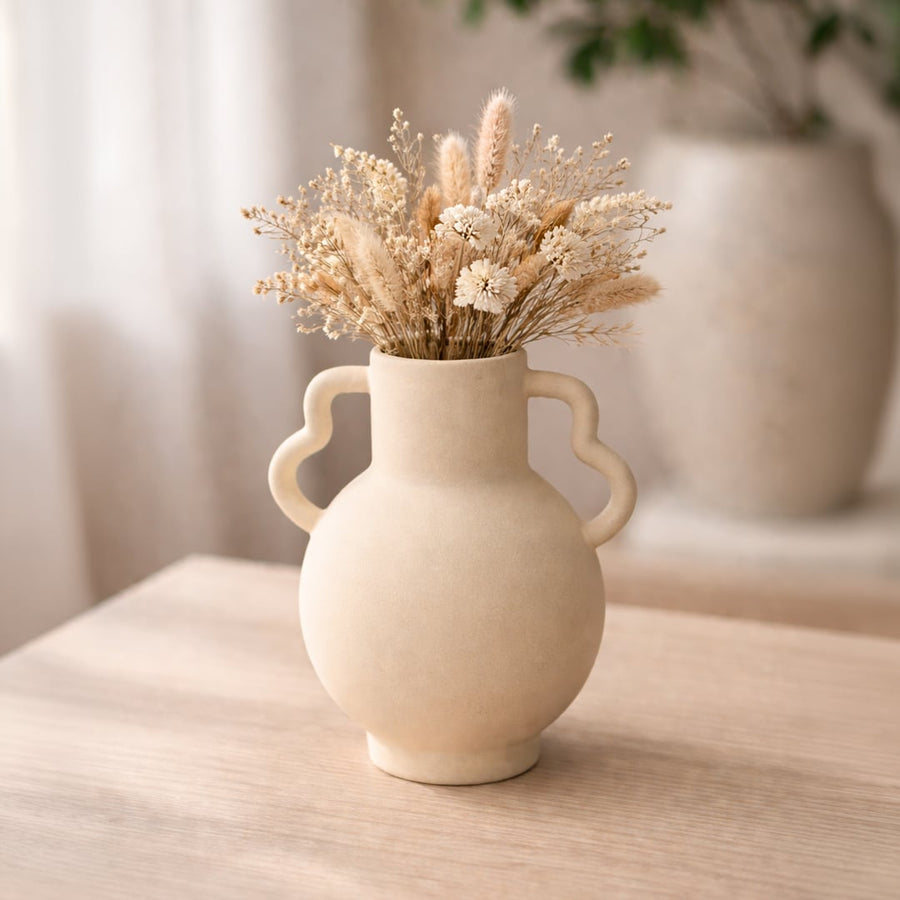 Beige ceramic double handle vase with dried stems placed on wooden table adding warm rustic charm to living room decor.