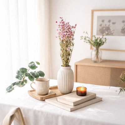 A beautiful pink and yellow dried wildflower bouquet in a white ribbed vase on a sunlit table with a burning candle.