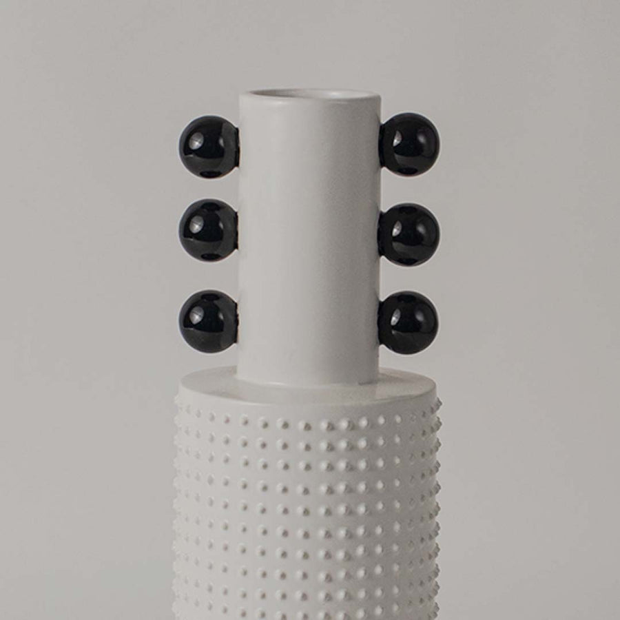 Closeup image of a white studded ceramic totem vase accented with rows of glossy black structural spheres on its neck.
