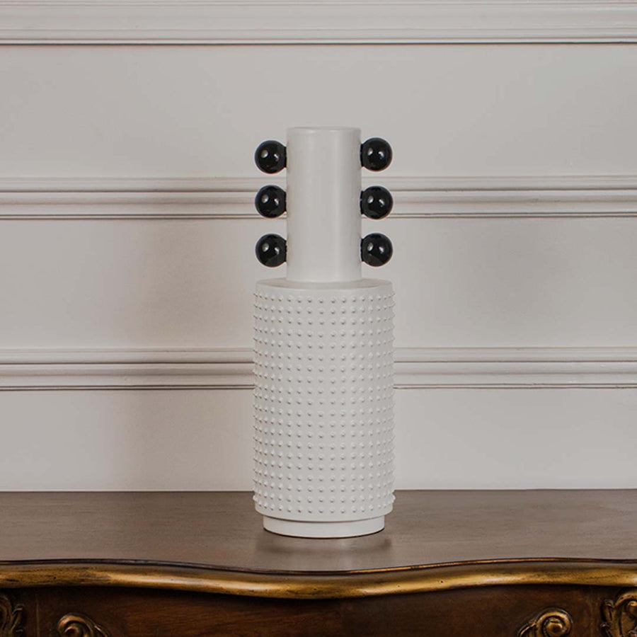 White studded ceramic totem vase with glossy black accent spheres displayed on a classic wooden console table for styling.