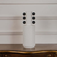 White studded ceramic totem vase with glossy black accent spheres displayed on a classic wooden console table for styling.