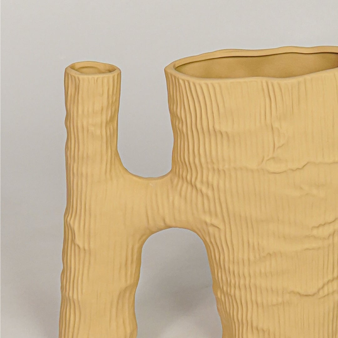 Closeup of beige ceramic vase with textured wood inspired finish for artistic tabletop and shelf decor styling.