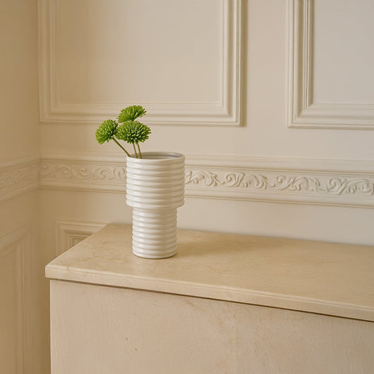 Elegant white ceramic vase with green chrysanthemum stems placed on a beige cabinet styled in a modern minimal home interior.