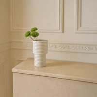 Elegant white ceramic vase with green chrysanthemum stems placed on a beige cabinet styled in a modern minimal home interior.