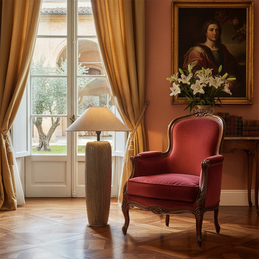 Tall textured ceramic floor lamp with a wide beige shade placed beside a classic red armchair creating a warm elegant accent in a luxurious living room.