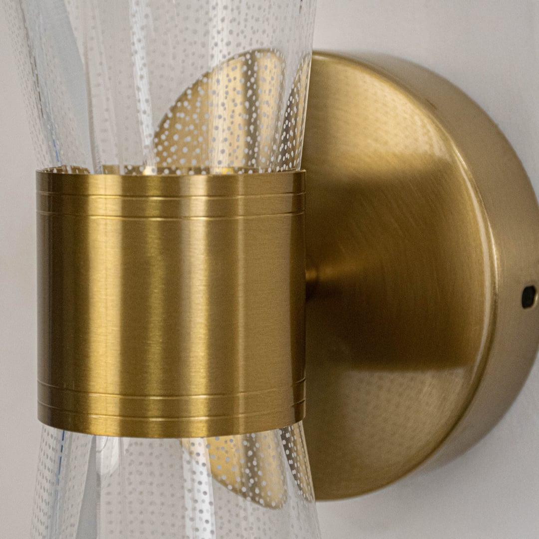 Closeup of gold wall light with sculpted clear glass shade highlighting curved design and fine textured detailing.
