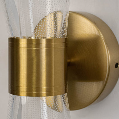 Closeup of gold wall light with sculpted clear glass shade highlighting curved design and fine textured detailing.