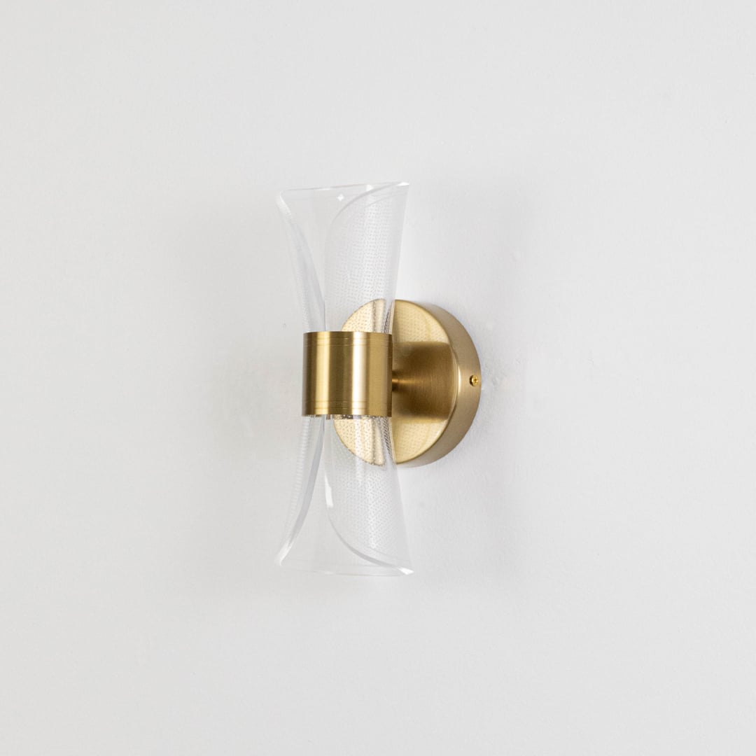 Gold wall light with sculpted clear glass shade shown on a bright white background with lights off for clarity.