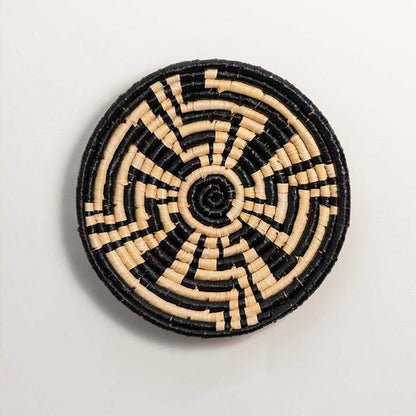 Round handcrafted black and cream seagrass wall basket with geometric sunburst labyrinth pattern on white background.
