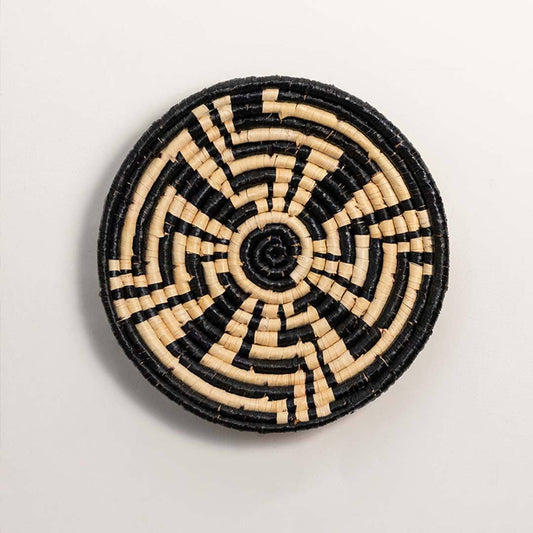 Round handcrafted black and cream seagrass wall basket with geometric sunburst labyrinth pattern on white background.