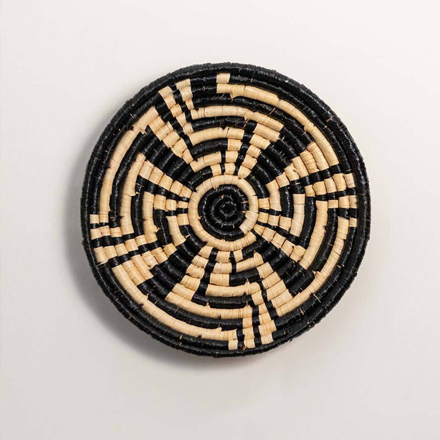 Round handcrafted black and cream seagrass wall basket with geometric sunburst labyrinth pattern on white background.