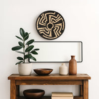 Medium black and beige woven wall basket hanging above a wooden console table with green rubber plant for modern home decor.