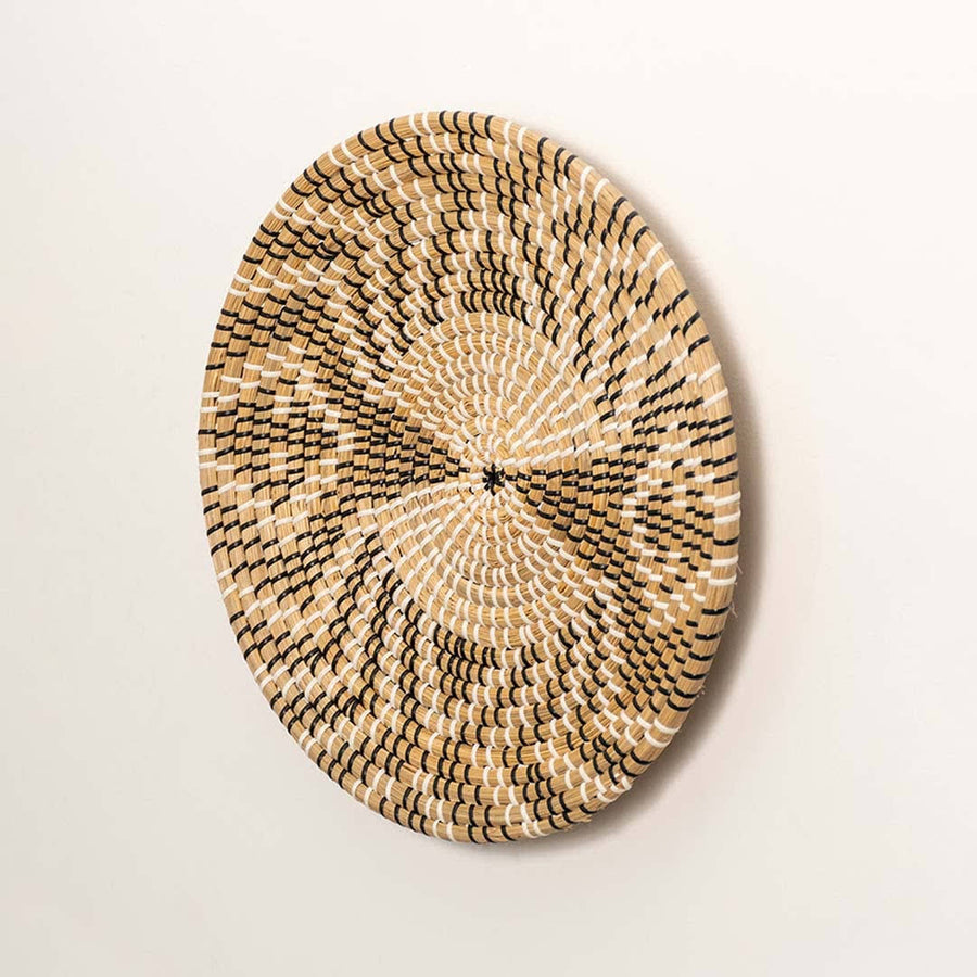 Side view of handcrafted black and natural seagrass wall basket with abstract geometric radial pattern for boho wall decor.