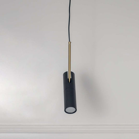 Black cylindrical pendant light with gold accent and hanging cord placed against neutral wall background highlighting sleek contemporary lighting design.