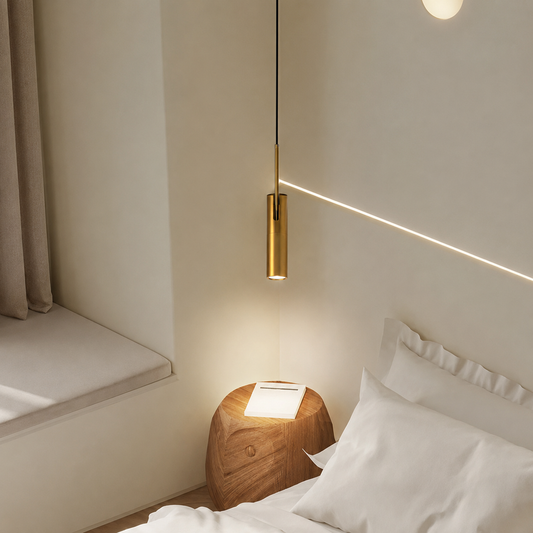 A modern cylindrical gold pendant light hanging over a bed in a minimalist bedroom setting, casting a warm glow and a light strip on the wall.