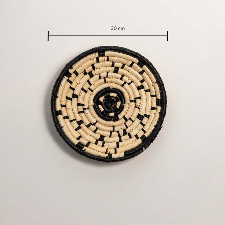 A handwoven natural and black rattan wall decor plate displayed on a white background with a clear diameter of 30 cm for accurate wall decor measurement and placement.