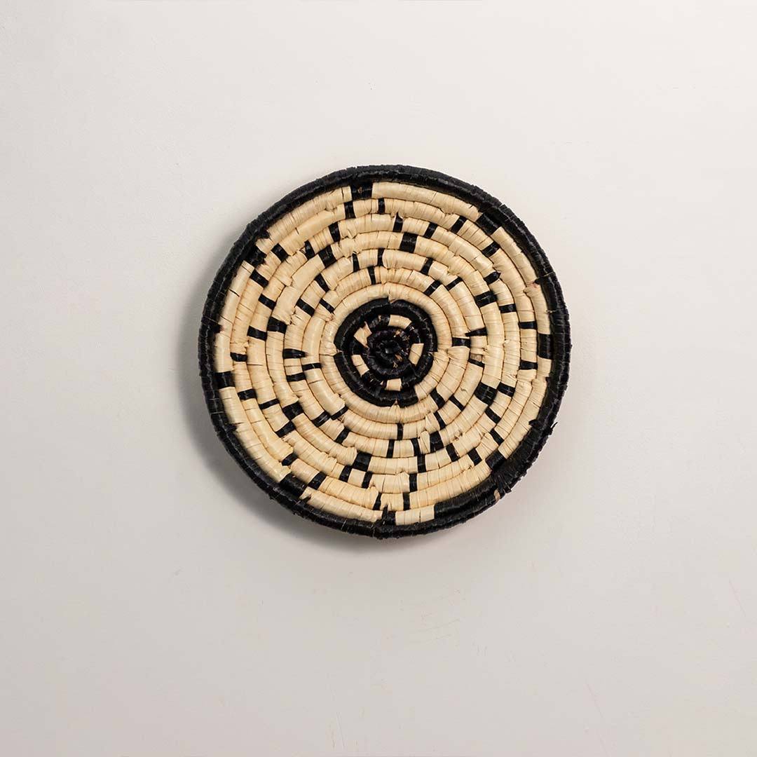 Round woven black and cream seagrass wall basket with geometric abstract dotted line pattern on white background image.