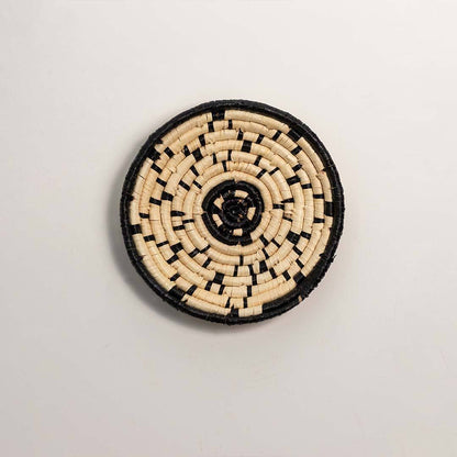 Round woven black and cream seagrass wall basket with geometric abstract dotted line pattern on white background image.