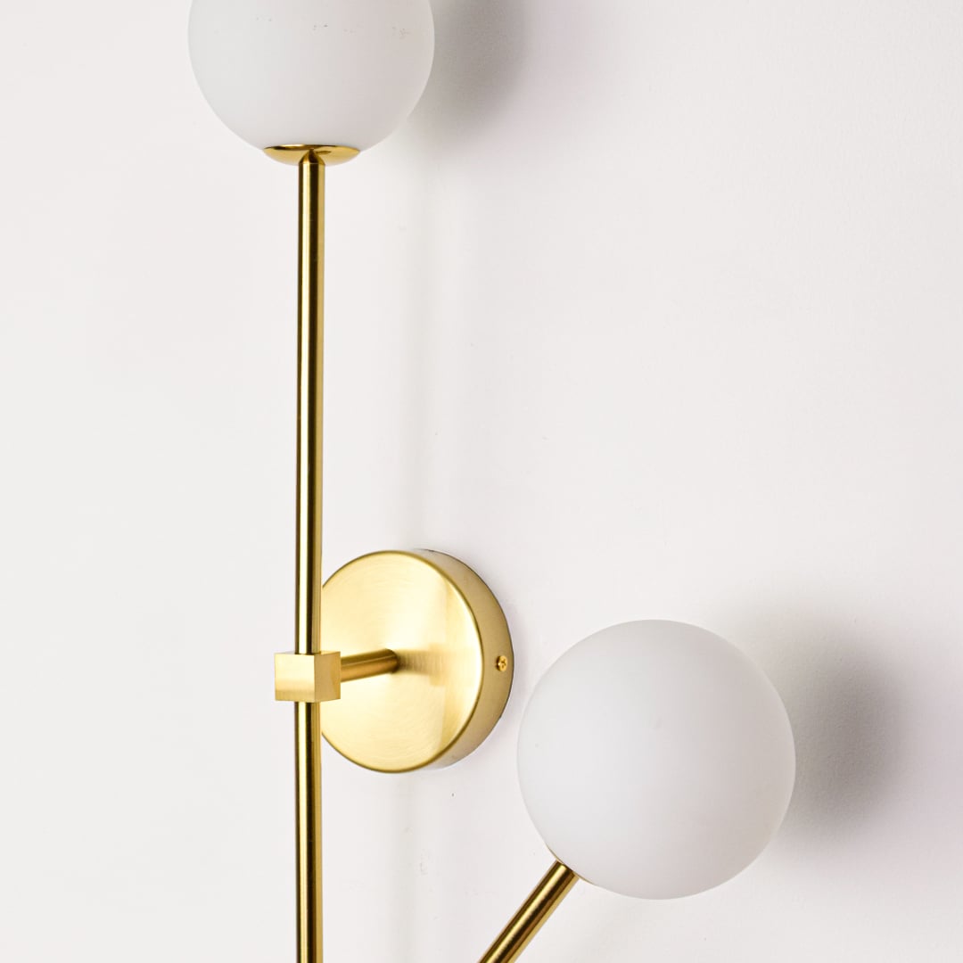 Gold metal wall sconce closeup showing white glass globe shades and polished finish for contemporary interior accent lighting.