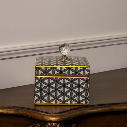 Ceramic storage jar with gold geometric design and crystal lid placed on wooden table against neutral wall background enhancing elegant decorative home styling.