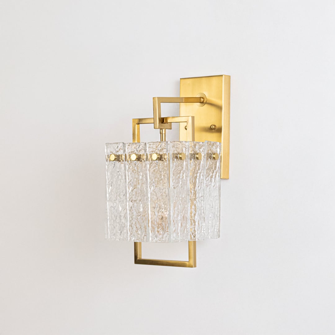 Minimalist gold wall sconce with textured glass shade shown switched off against plain white background for product photography.