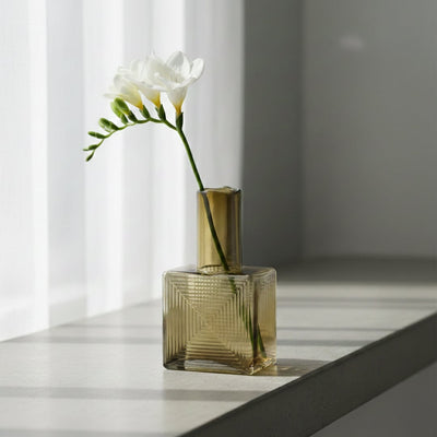 Amber glass decorative vase styled with fresh flowers by a window for elegant modern home decor arrangements.