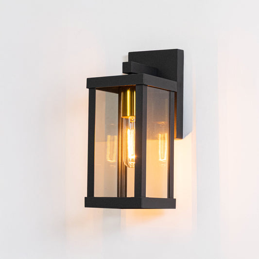 Black metal outdoor wall light on white background with clear glass shade for modern patio lighting decor.