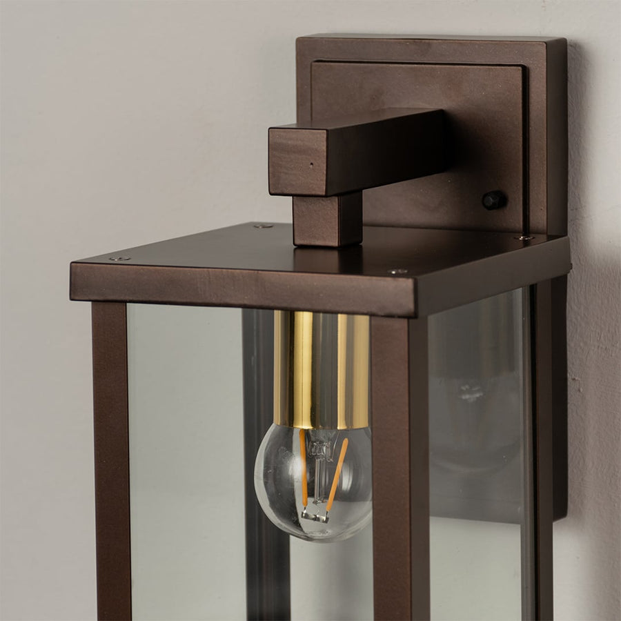 Closeup of metal wall lantern with clear glass detailing showing bulb design and refined outdoor lighting style.