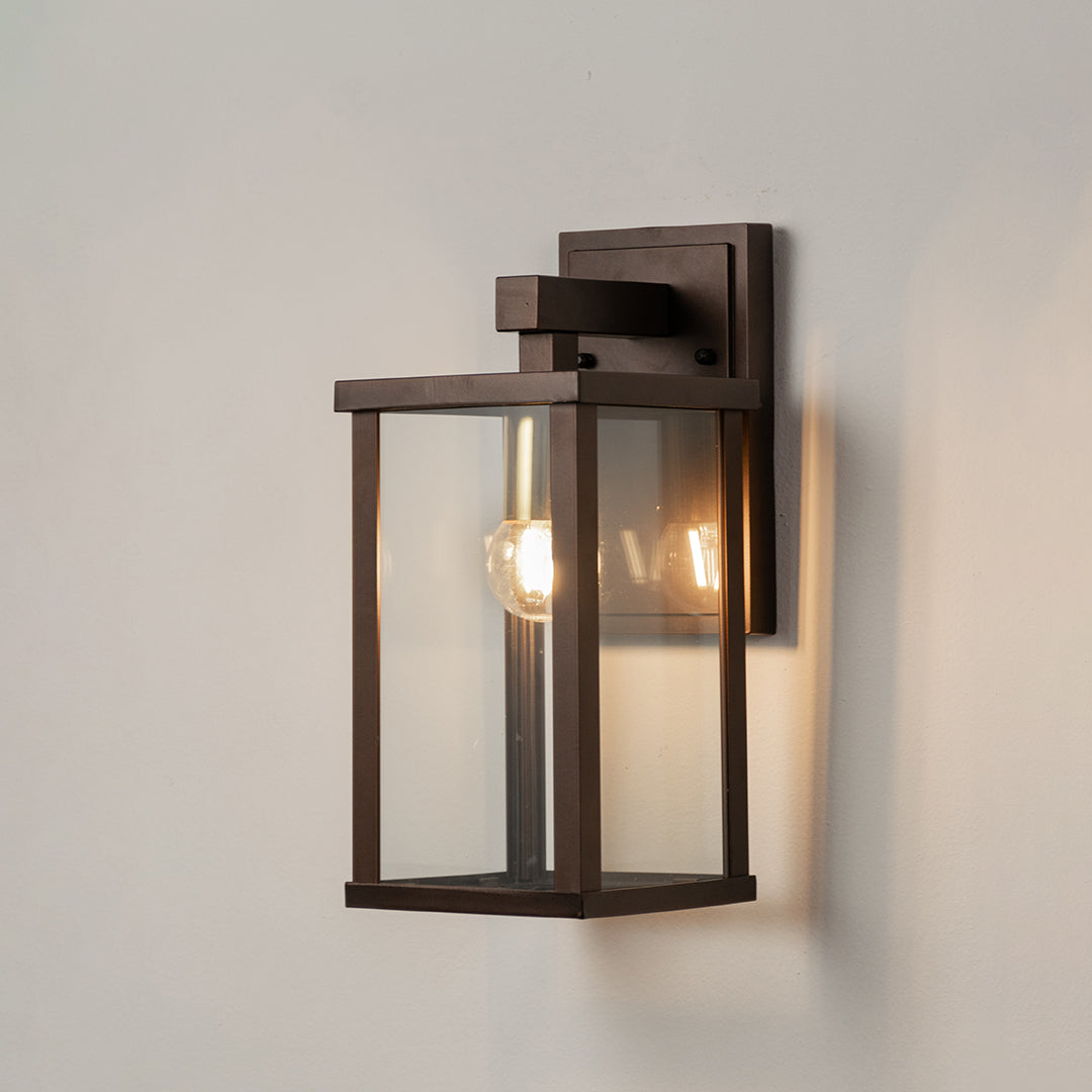 Black metal outdoor wall light on white background with clear glass shade for minimalist patio lighting decor.