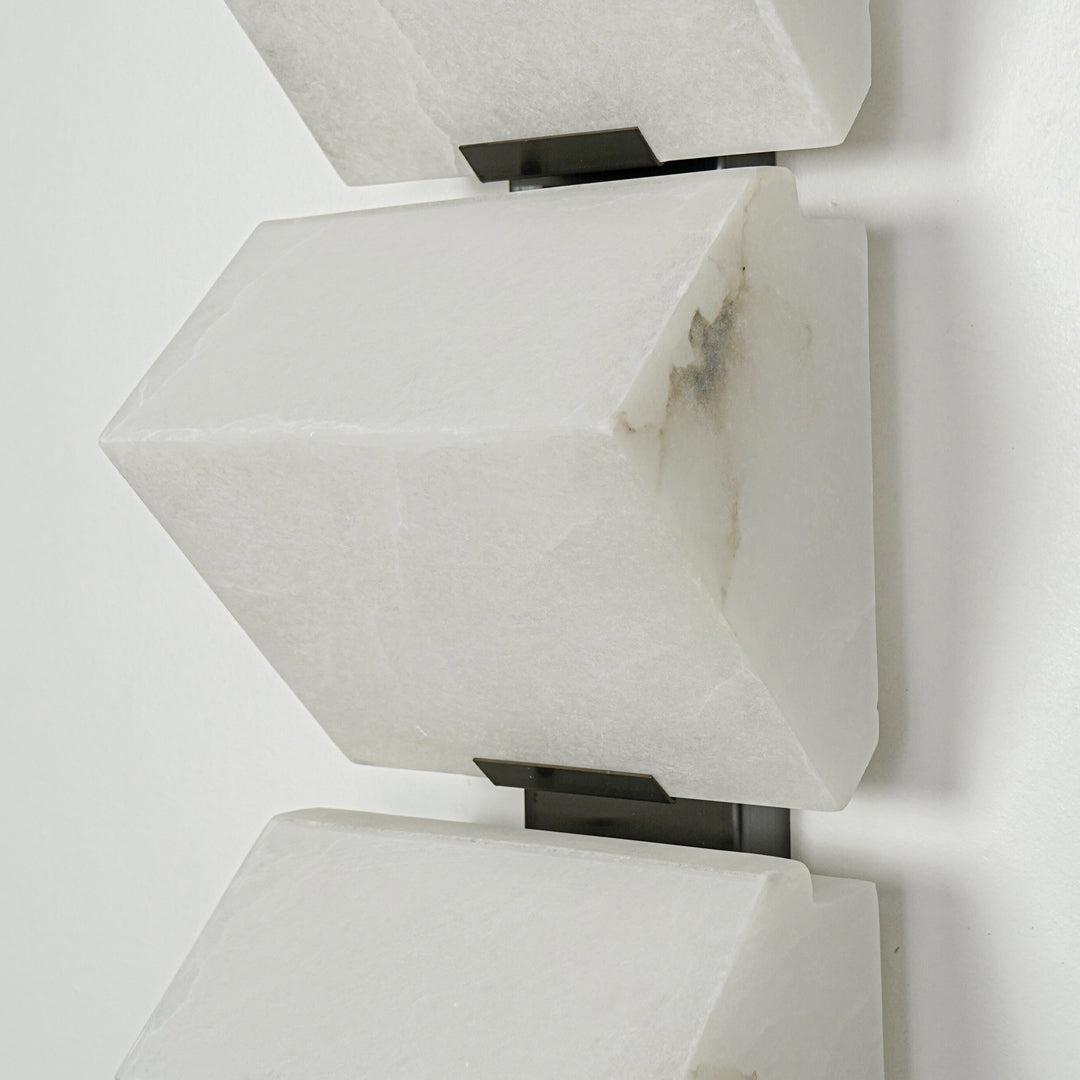 Close view of white metal wall sconce with angular geometric shade showcasing minimalist modern lighting design on clean background.