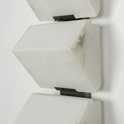Close view of white metal wall sconce with angular geometric shade showcasing minimalist modern lighting design on clean background.