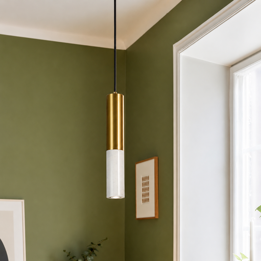 A modern pendant light with a brushed gold cylindrical upper section and a frosted white lower shade, hanging in a room with an olive green wall and white window trim.