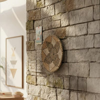 Handcrafted round wall decor in natural fiber finish mounted on stone wall adding earthy texture and warm accent to modern living space.