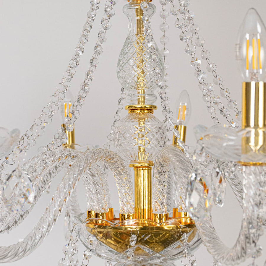 Closeup of chandelier with crystal arms and gold finish highlighting detailed glass design and lighting.