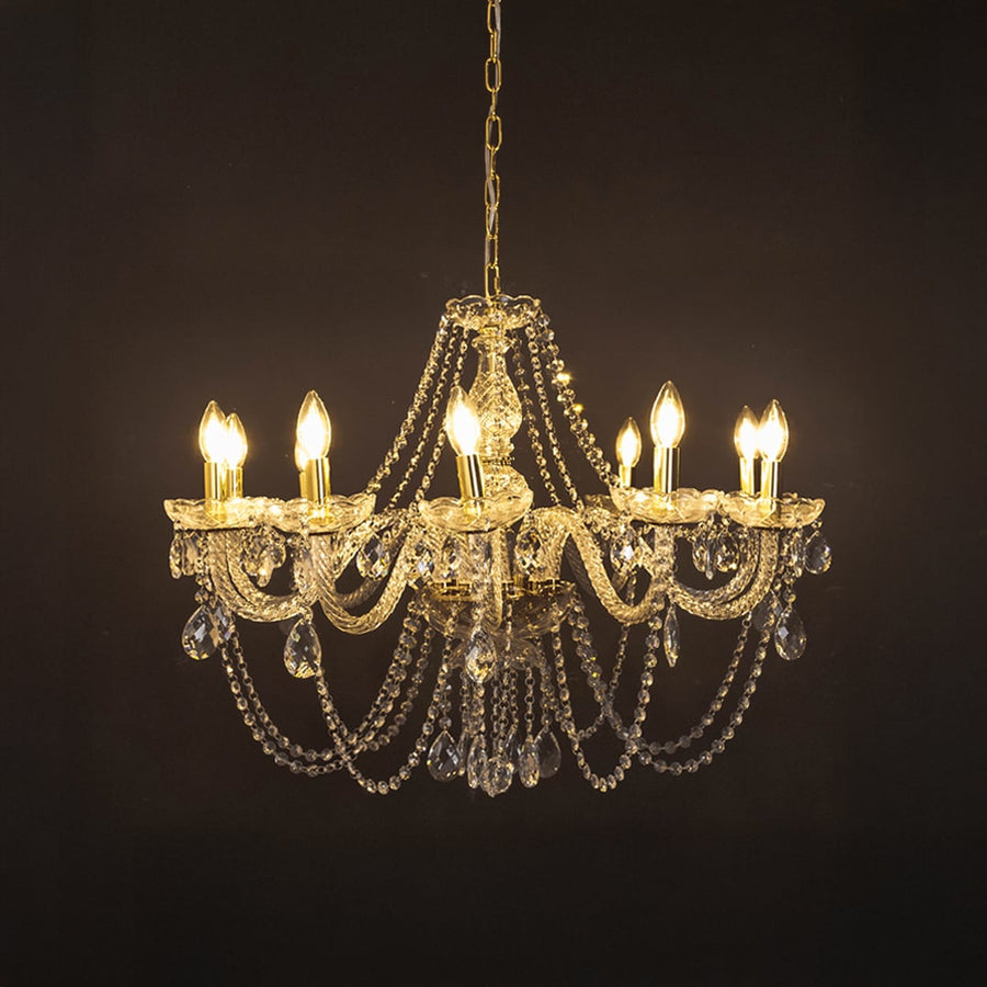 Crystal chandelier with gold base illuminated against black background showing luxury lighting design.