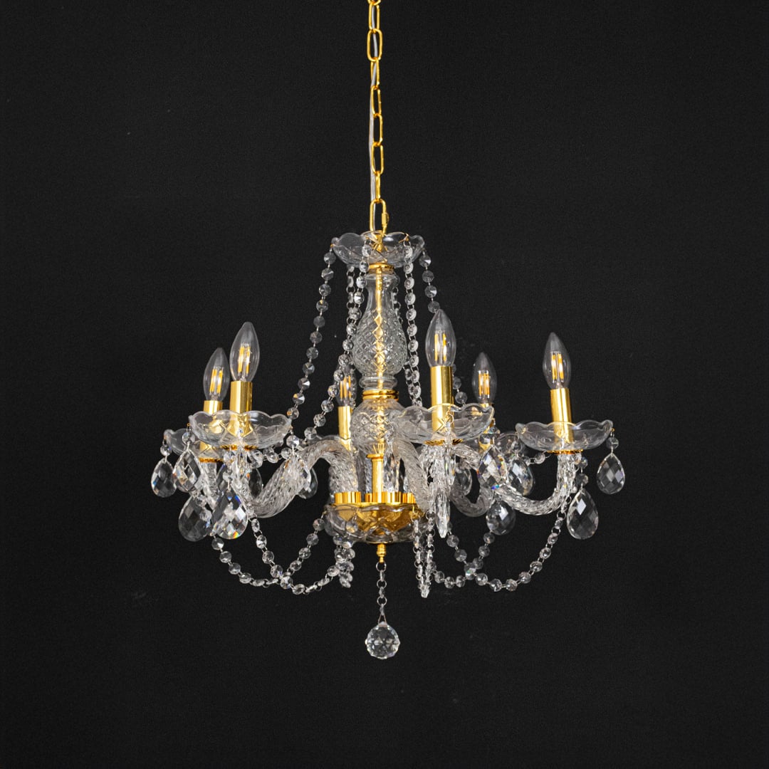 Chandelier with gold base and crystal design turned off against black background for modern interior styling.