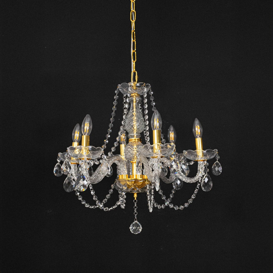 Chandelier with gold base and crystal design turned off against black background for modern interior styling.