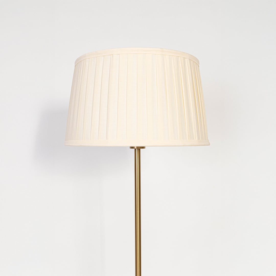 Closeup of pleated white lampshade with golden lamp base showing fine fabric texture and warm light glow.