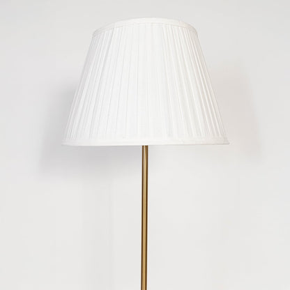 Closeup of golden metal floor lamp with pleated white shade highlighting premium lighting design for home interiors.
