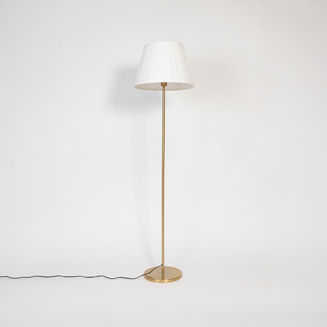 Golden stand floor lamp with pleated white shade displayed switched off against plain white background.