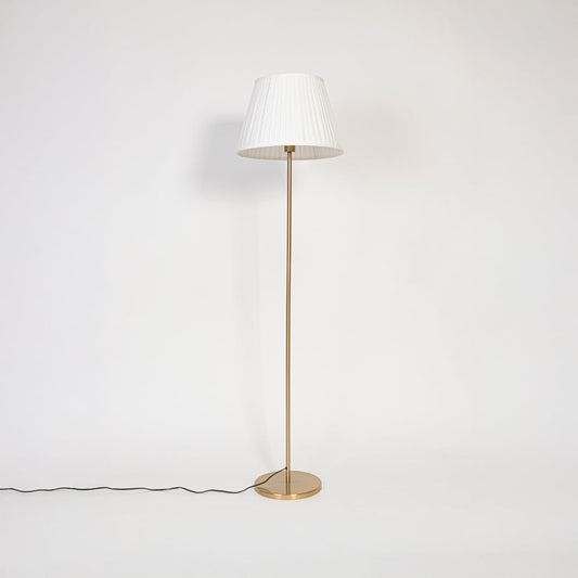 Golden stand floor lamp with pleated white shade displayed switched off against plain white background.