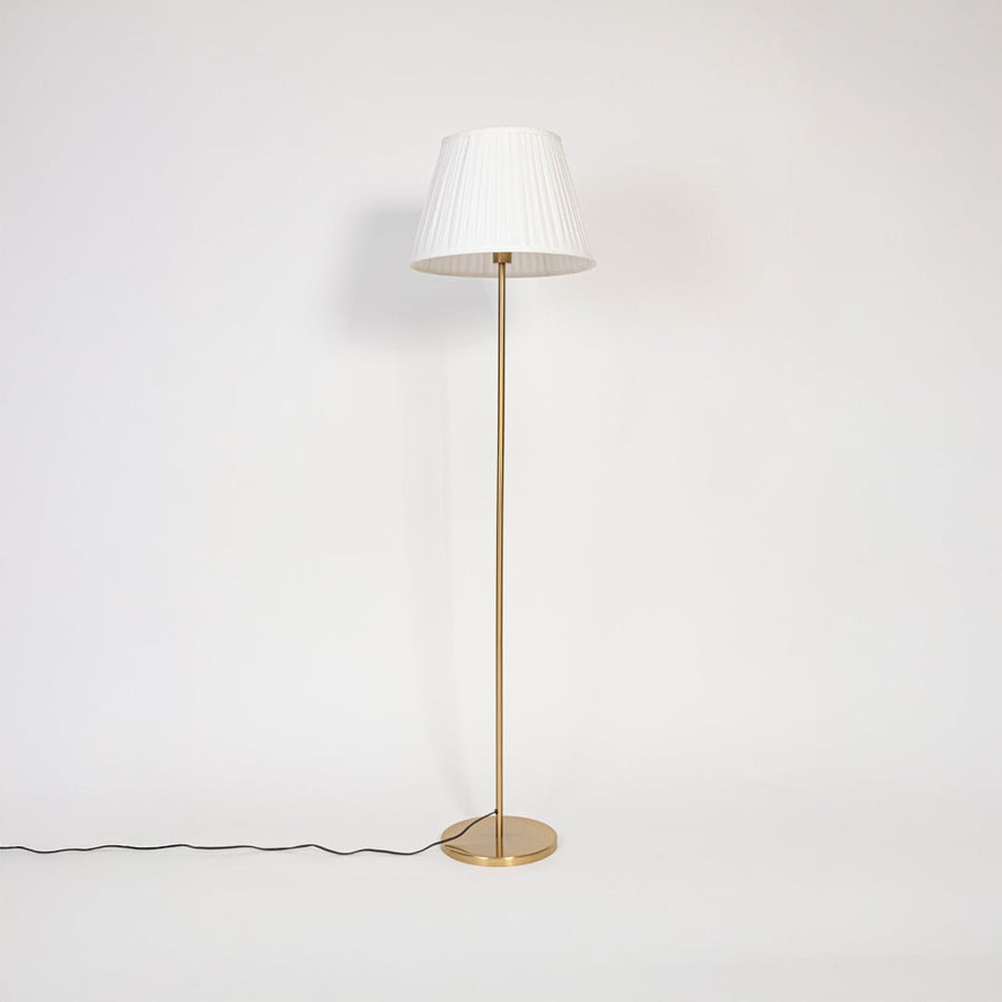 Golden stand floor lamp with pleated white shade displayed switched off against plain white background.